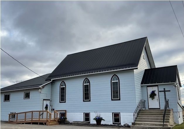 Shiloh Community Church building with white siding, a dark metal roof, arched windows, entrance stairs, and an accessibility ramp